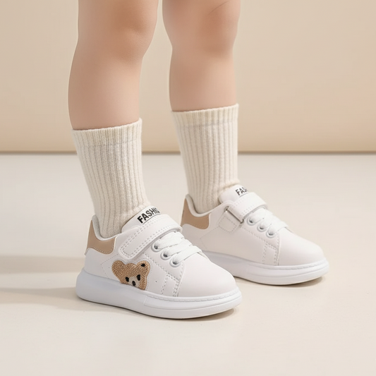 White sneakers with a bear design worn by a child on a neutral background