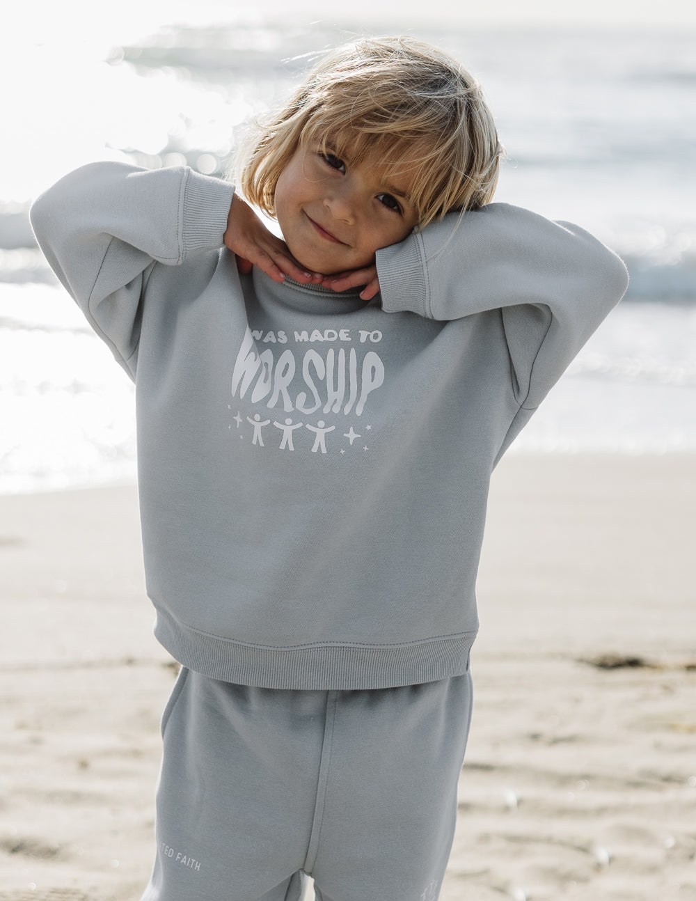 Child wearing a gray hoodie with text on a beach