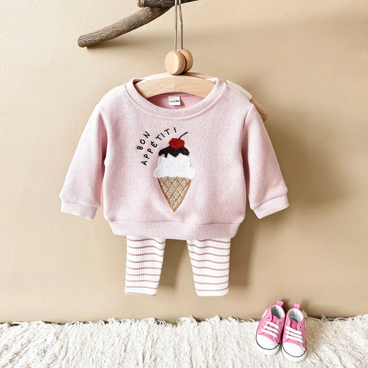 Pink baby outfit with ice cream design on a hanger against a beige wall.