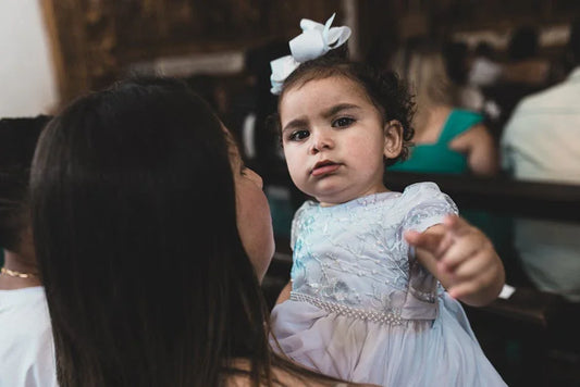 Heartwarming scene of a mother holding her cute baby girl in a white dress indoors.