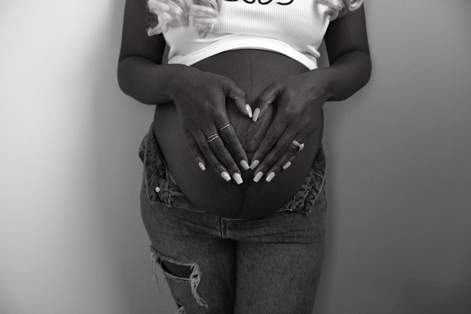 Black and white image of a pregnant woman holding her belly in a heart shape.