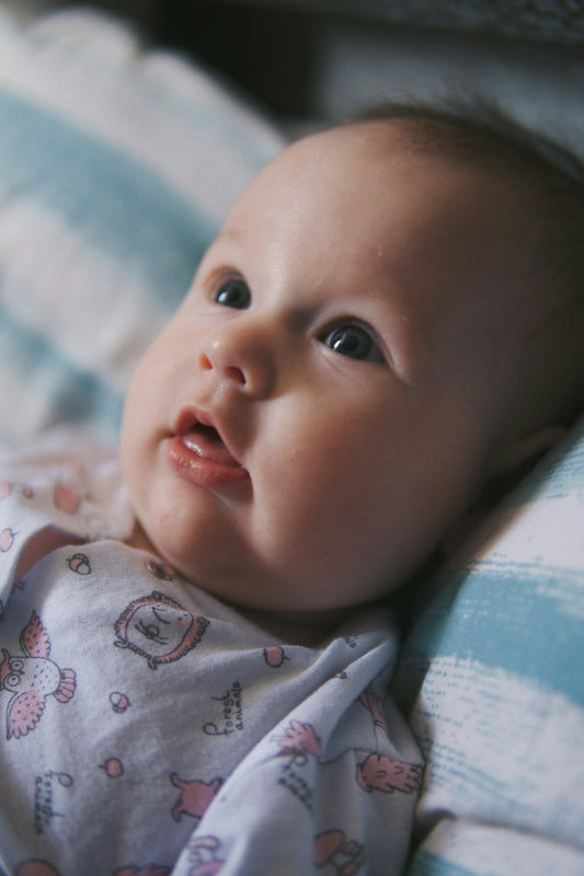 baby in white and blue onesie lying on bed
