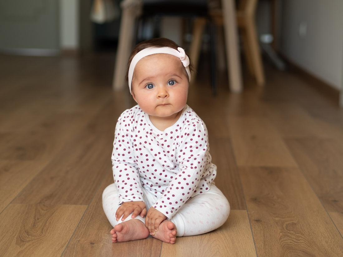 baby in white and black onesie lying on brown wooden floor