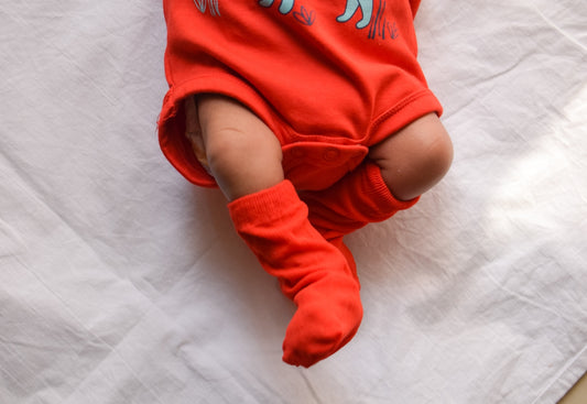 baby in red and white onesie lying on white textile