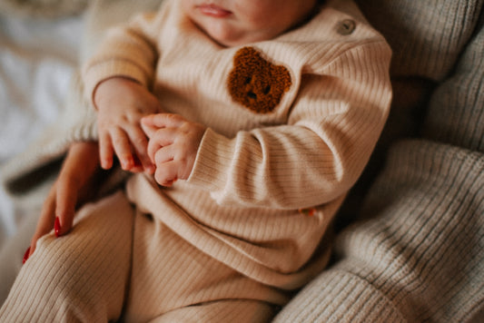 a baby is wearing a sweater and holding a teddy bear