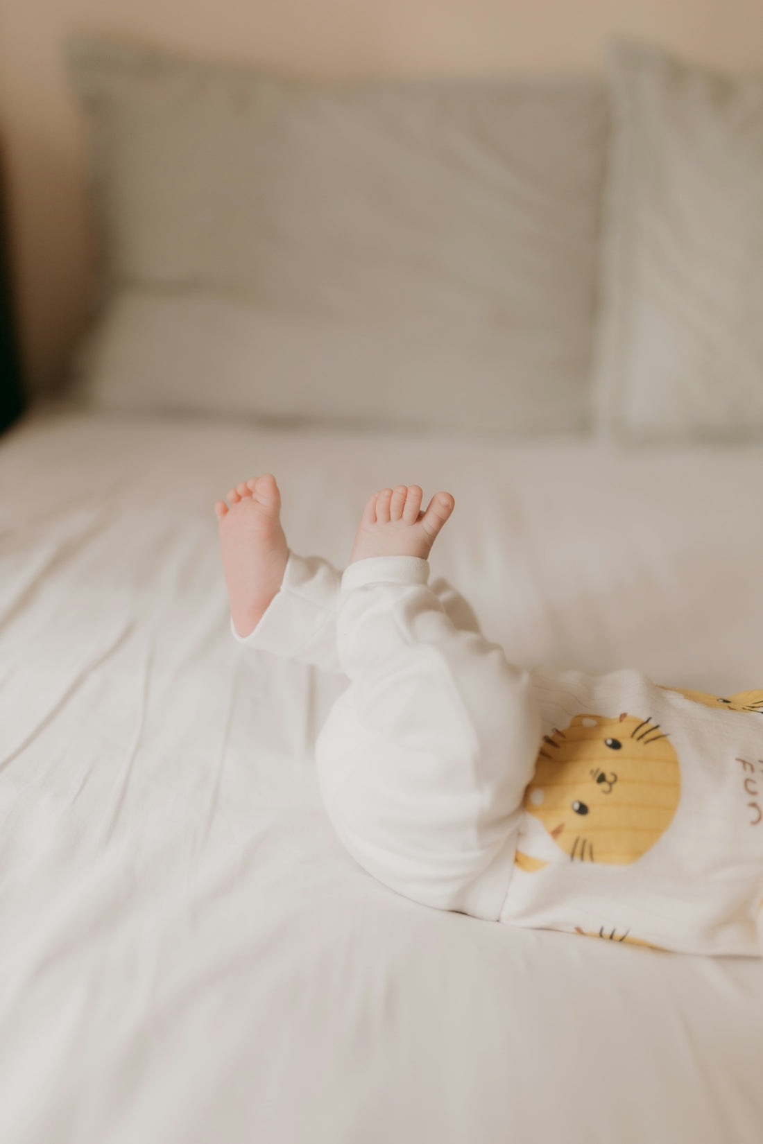 A baby lies on a bed with its feet up.