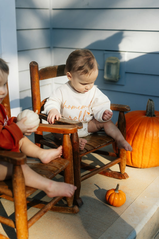 Baby sitting on rocking chair with pumpkins