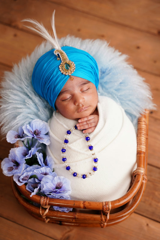 Newborn baby boy wearing a blue turban and necklace.