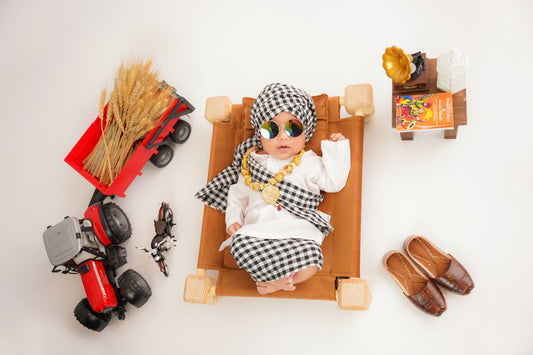 Baby dressed as a farmer with toy tractor and wheat.