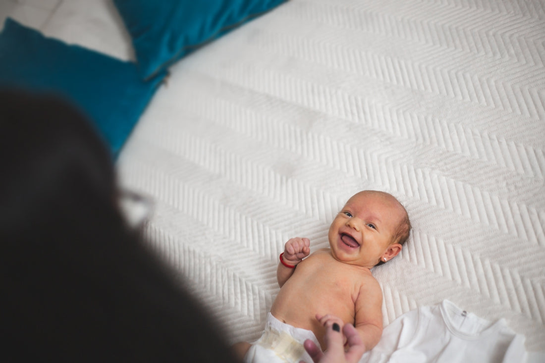 A happy newborn baby lying on a white textured bed.