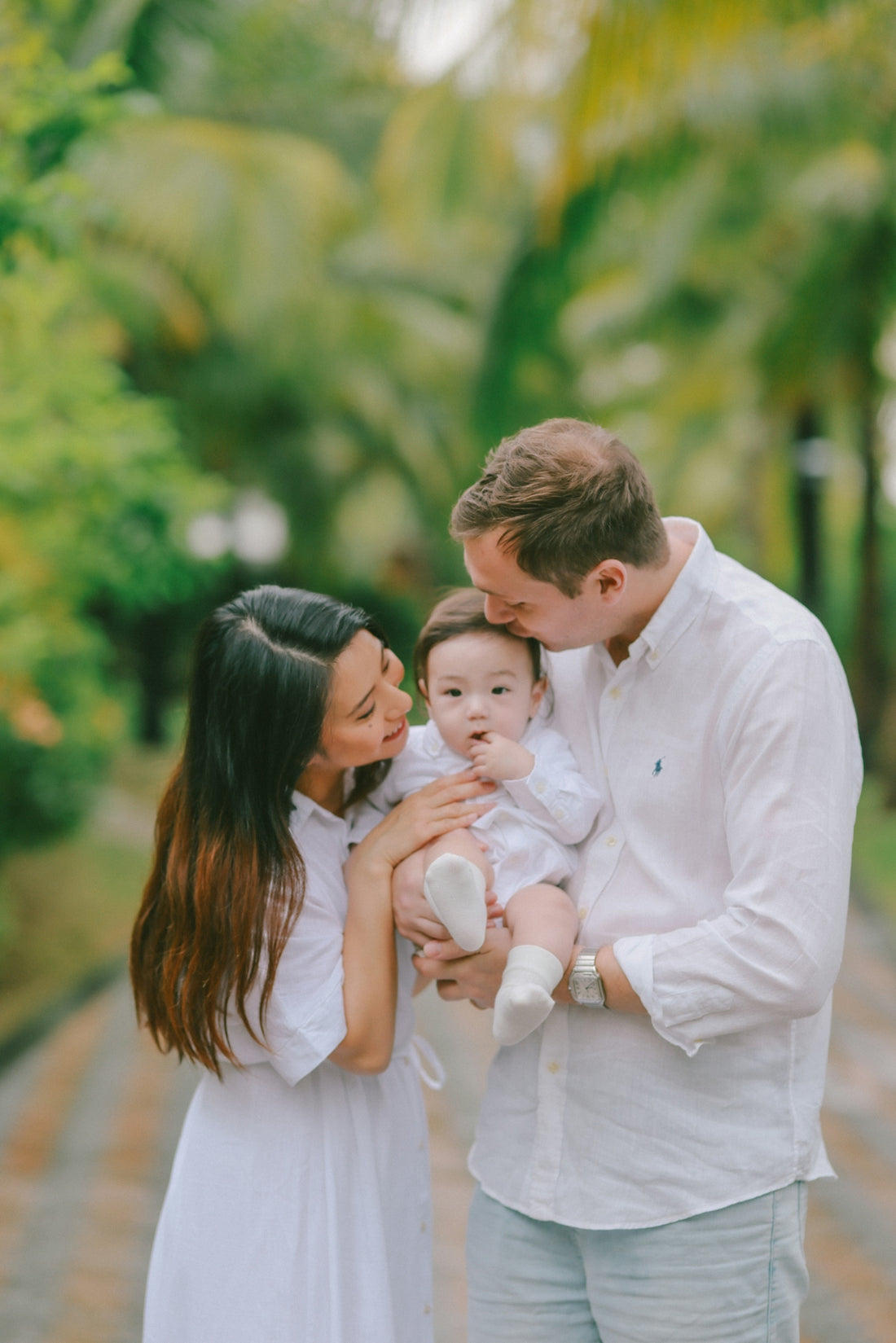 Parents holding their baby outdoors with lush greenery.