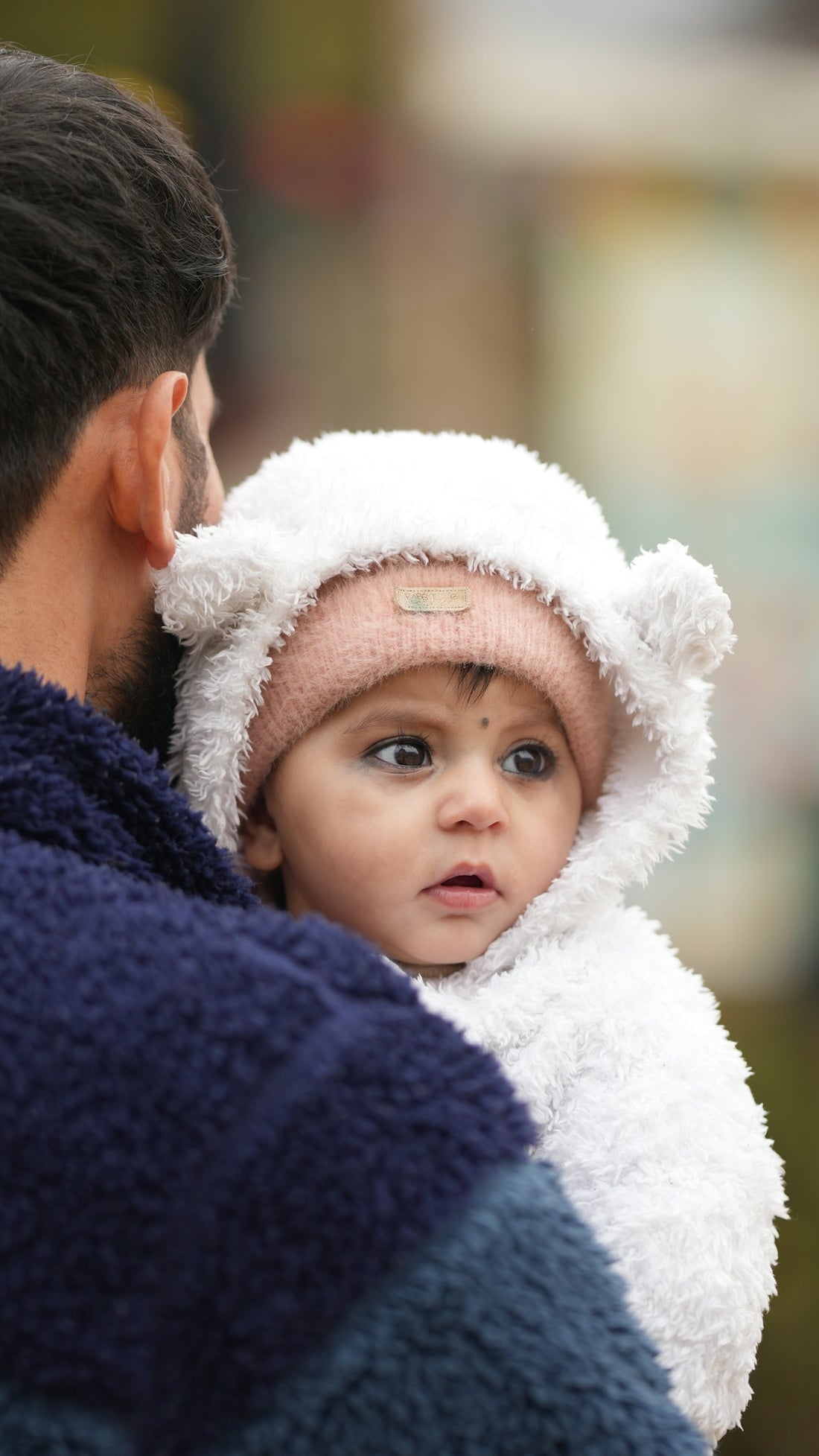 Father holding a baby in a fluffy white suit.