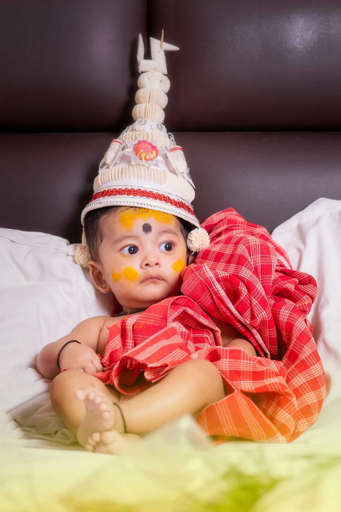 A baby wearing a traditional bengali outfit and headdress.