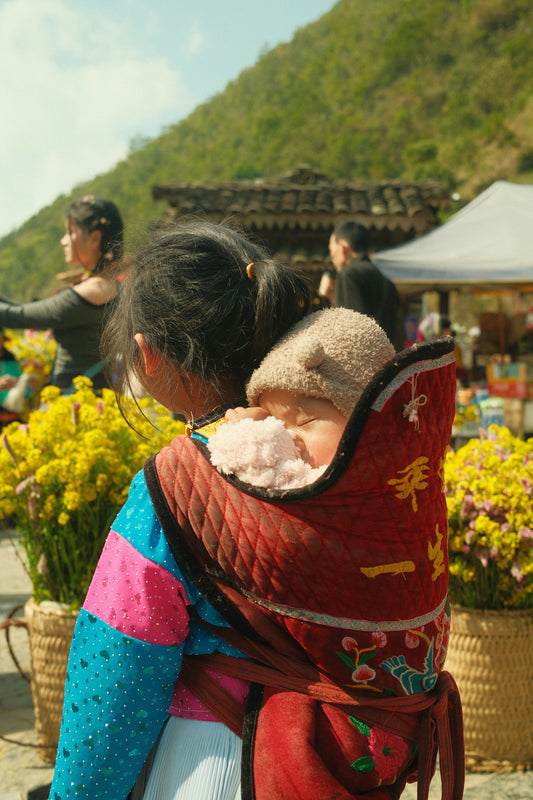 A child carries a sleeping baby on their back.
