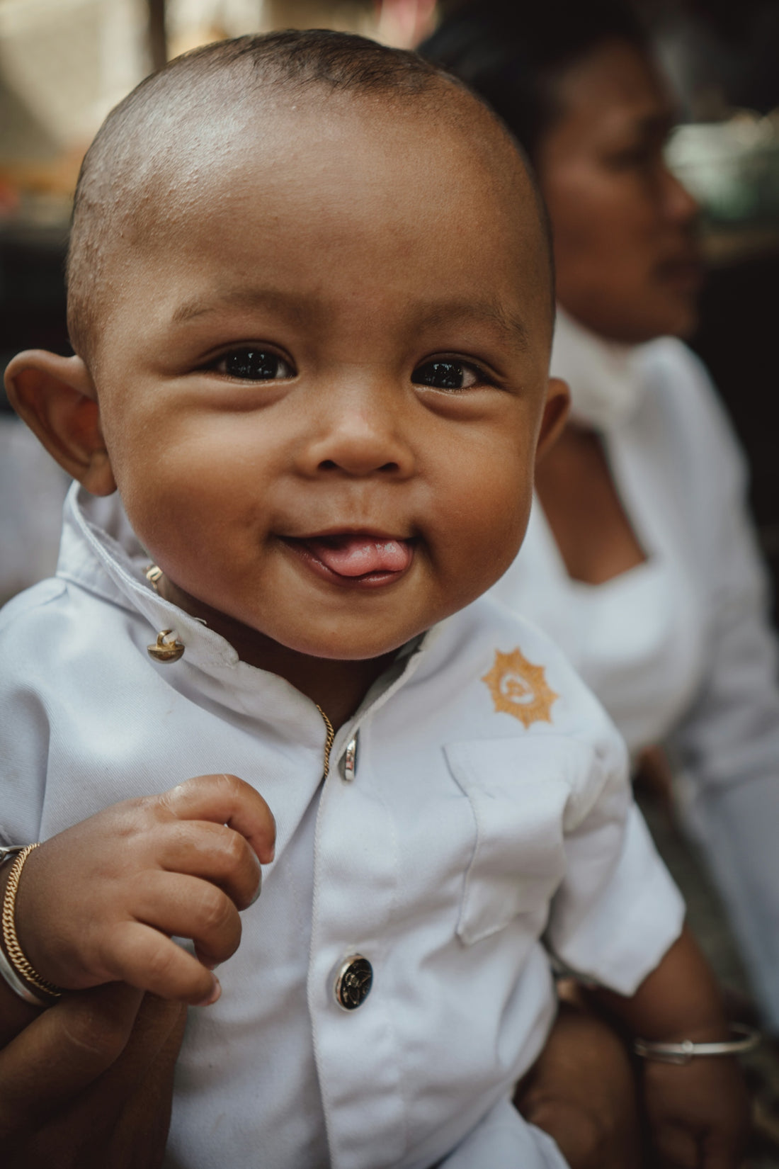A baby in a white outfit sticking its tongue out.