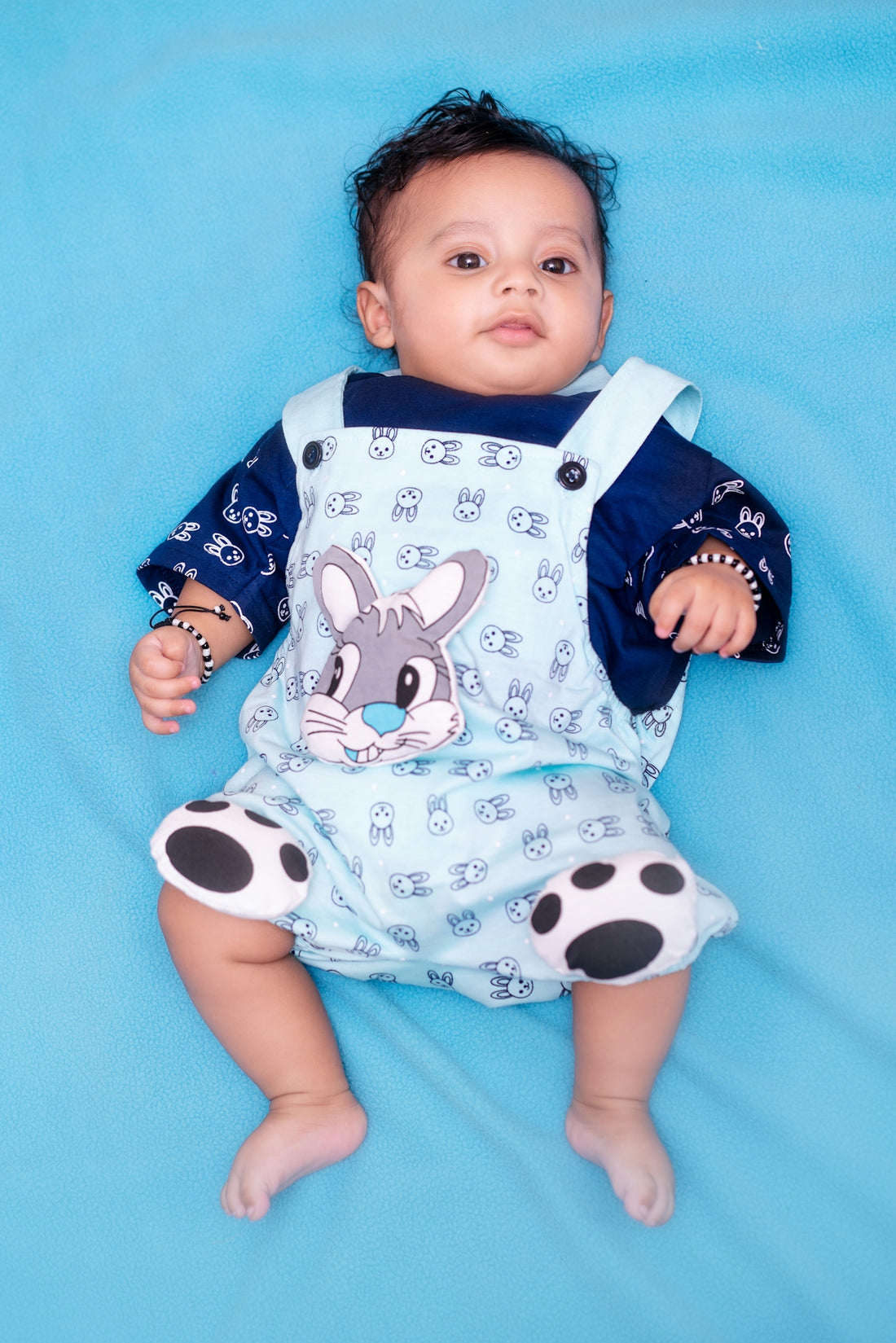 Adorable baby in blue bunny overalls on a blue background.