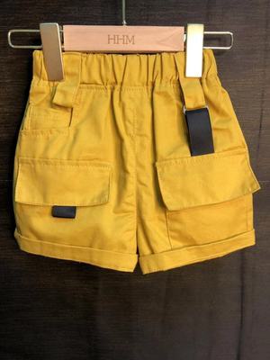 Mustard yellow toddler shorts with large front pockets and black buckle details on wooden hanger