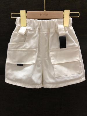 White children's cargo shorts with large side pockets on a wooden hanger against a dark background