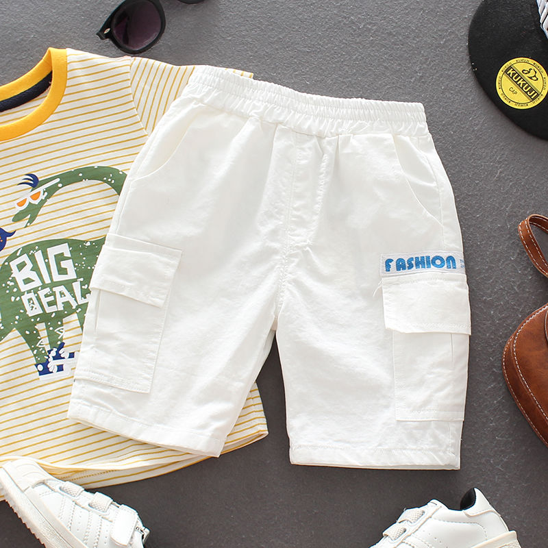 White kids cargo shorts with elastic waist and pockets, paired with striped dinosaur t-shirt and white sneakers