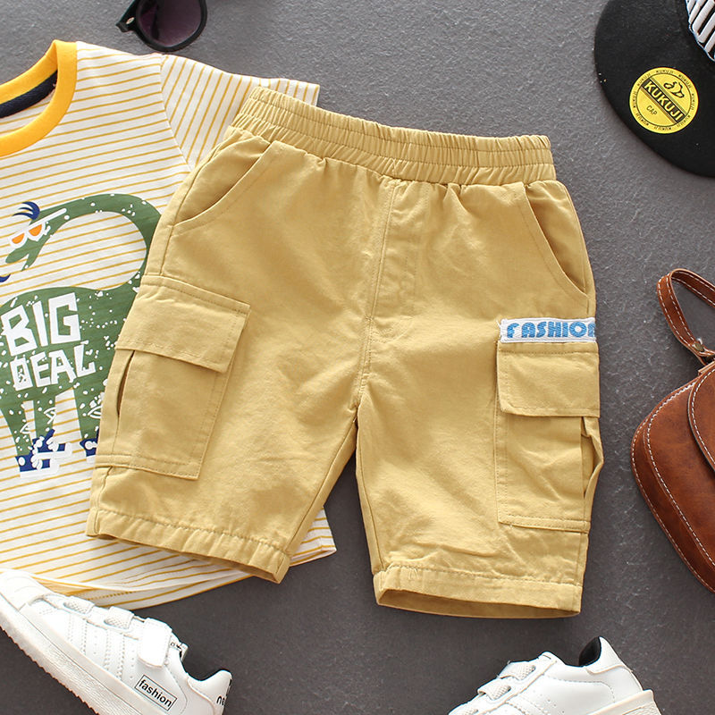 Kids yellow cargo shorts with pockets and elastic waistband, paired with striped dinosaur t-shirt and white sneakers
