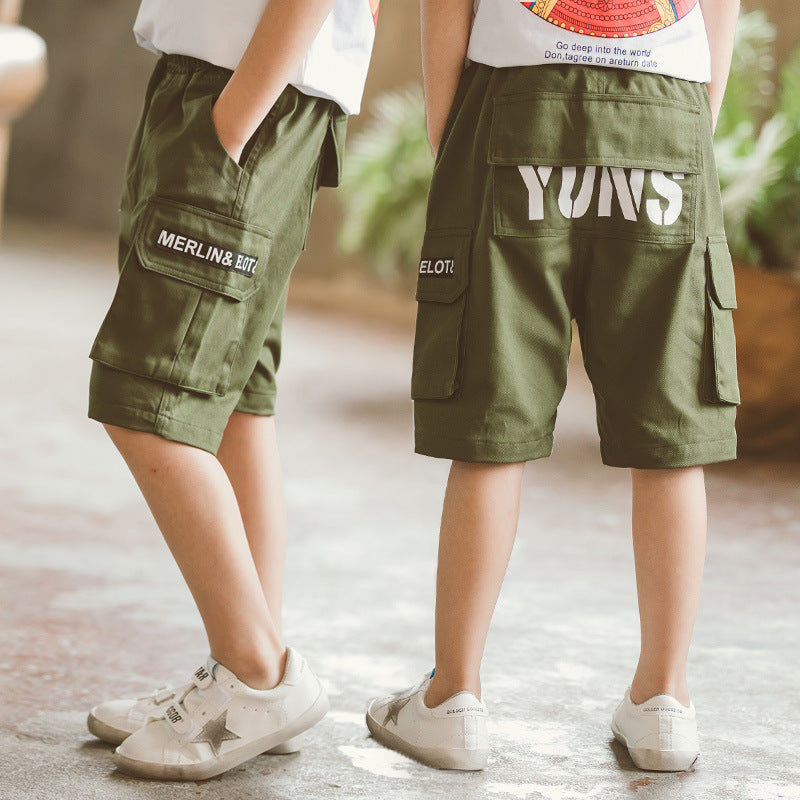 Two children wearing olive green cargo shorts with pockets and white sneakers indoors