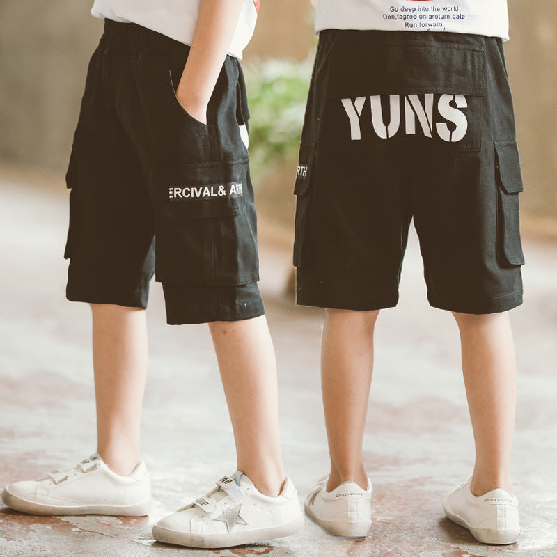 Two kids wearing black cargo shorts with text prints, paired with white sneakers in an indoor setting