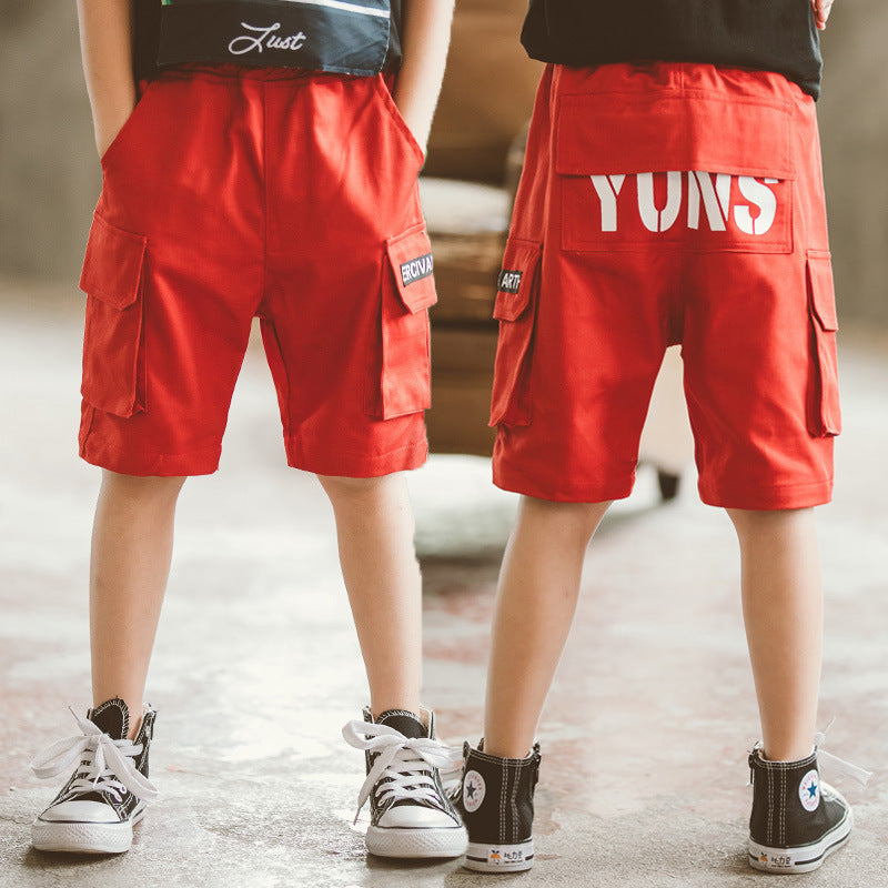 Front and back view of kids wearing bright red cargo shorts with black and white sneakers in indoor setting