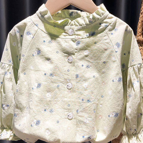 Light green button-up blouse with ruffled collar and small blue and white floral print on hanger