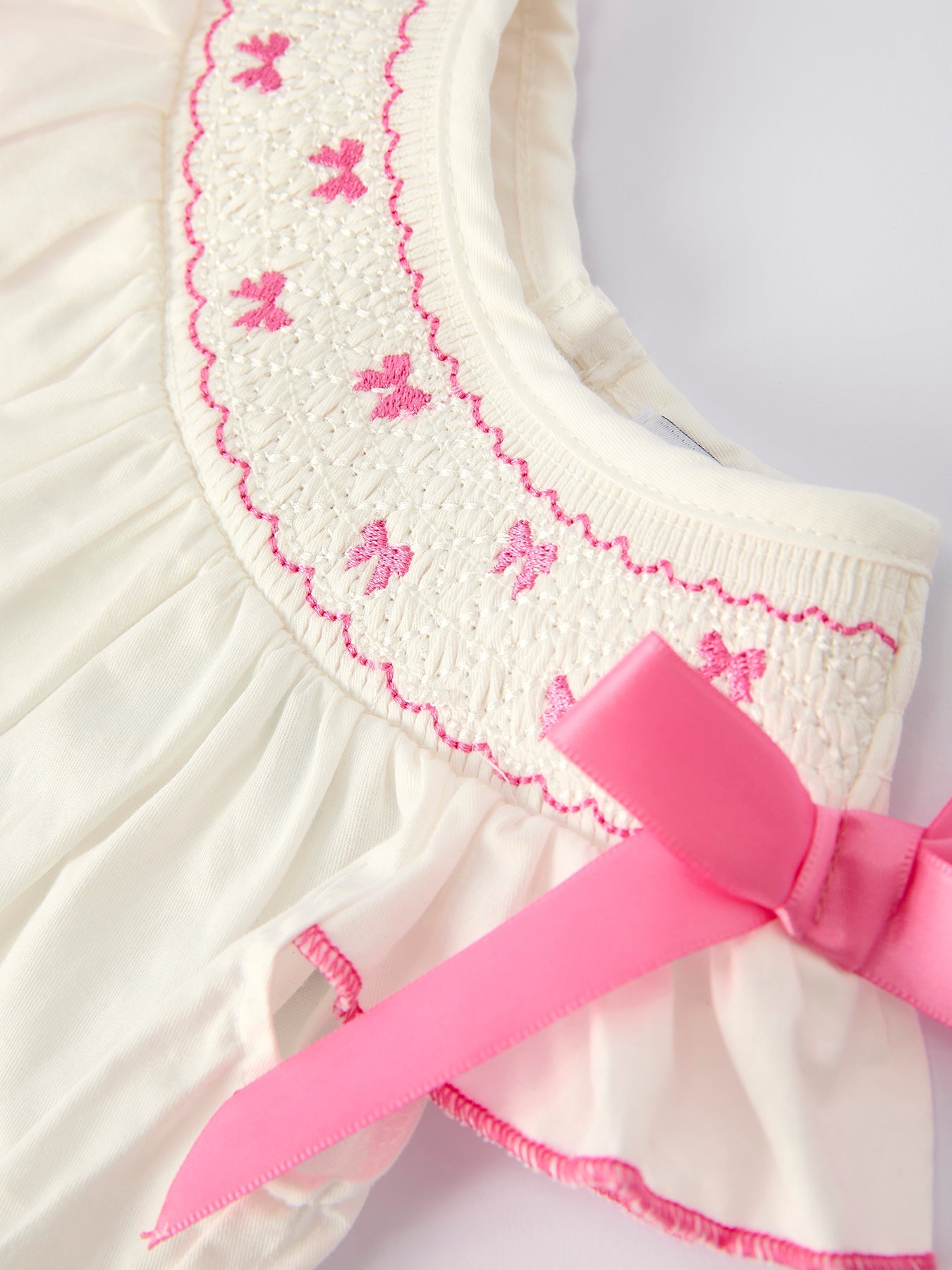 White dress with pink butterfly embroidery and a large pink bow on a white background