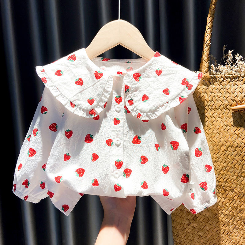 White baby blouse with red strawberry print, ruffled collar, and buttons on wooden hanger