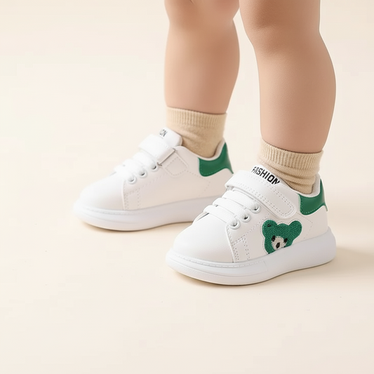 White sneakers with green bear designs worn by a child on a beige background