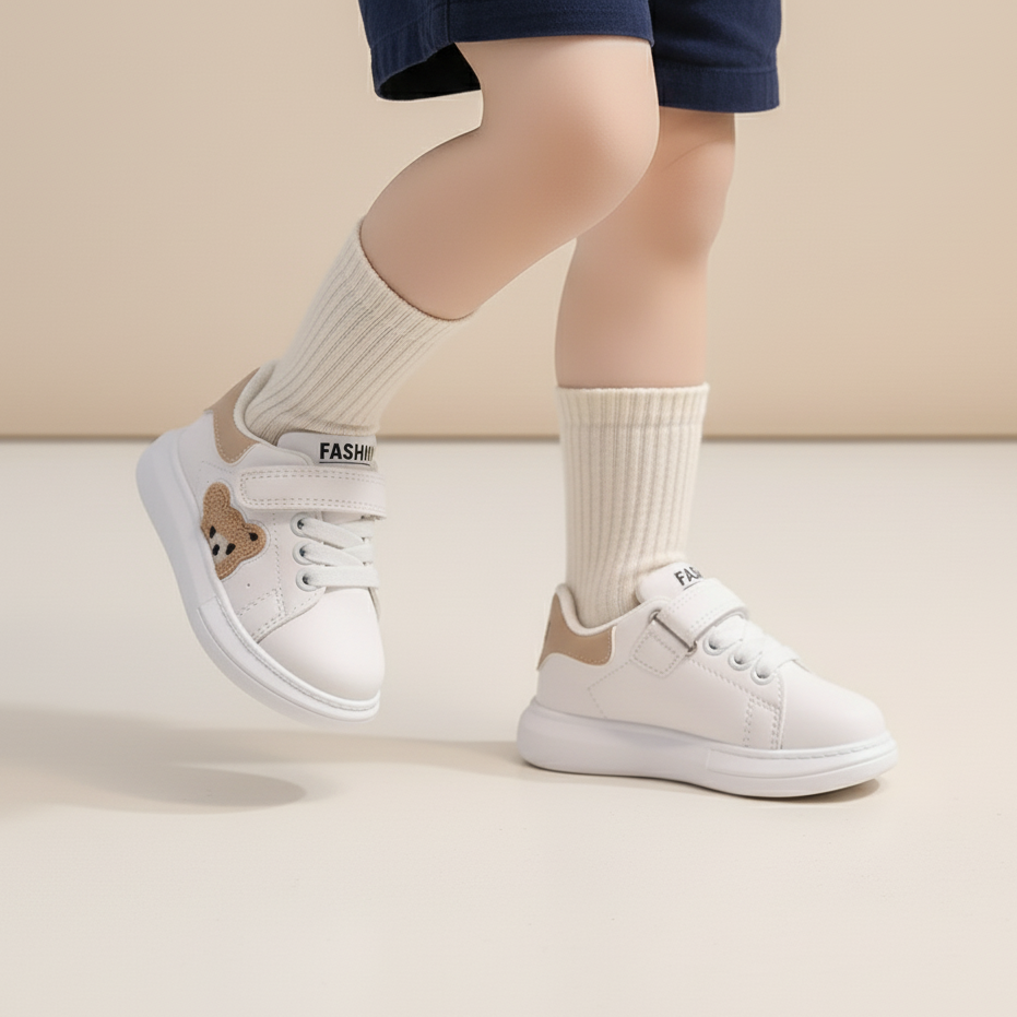 White sneakers with bear design and beige accents worn by a child on a neutral background
