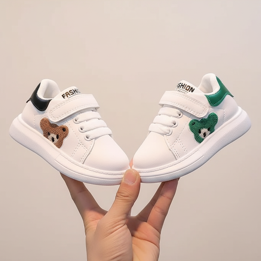 White children's sneakers with bear designs held by a hand against a neutral background