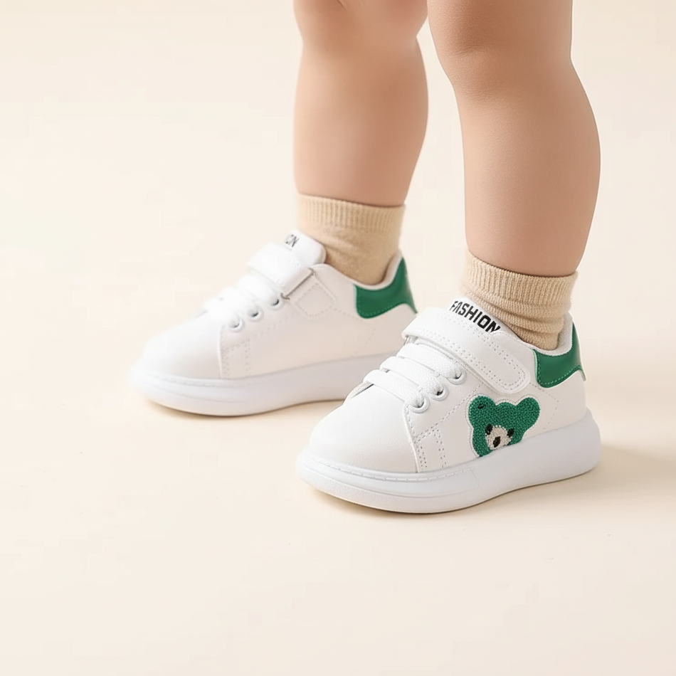 White sneakers with green bear designs worn by a child on a light background