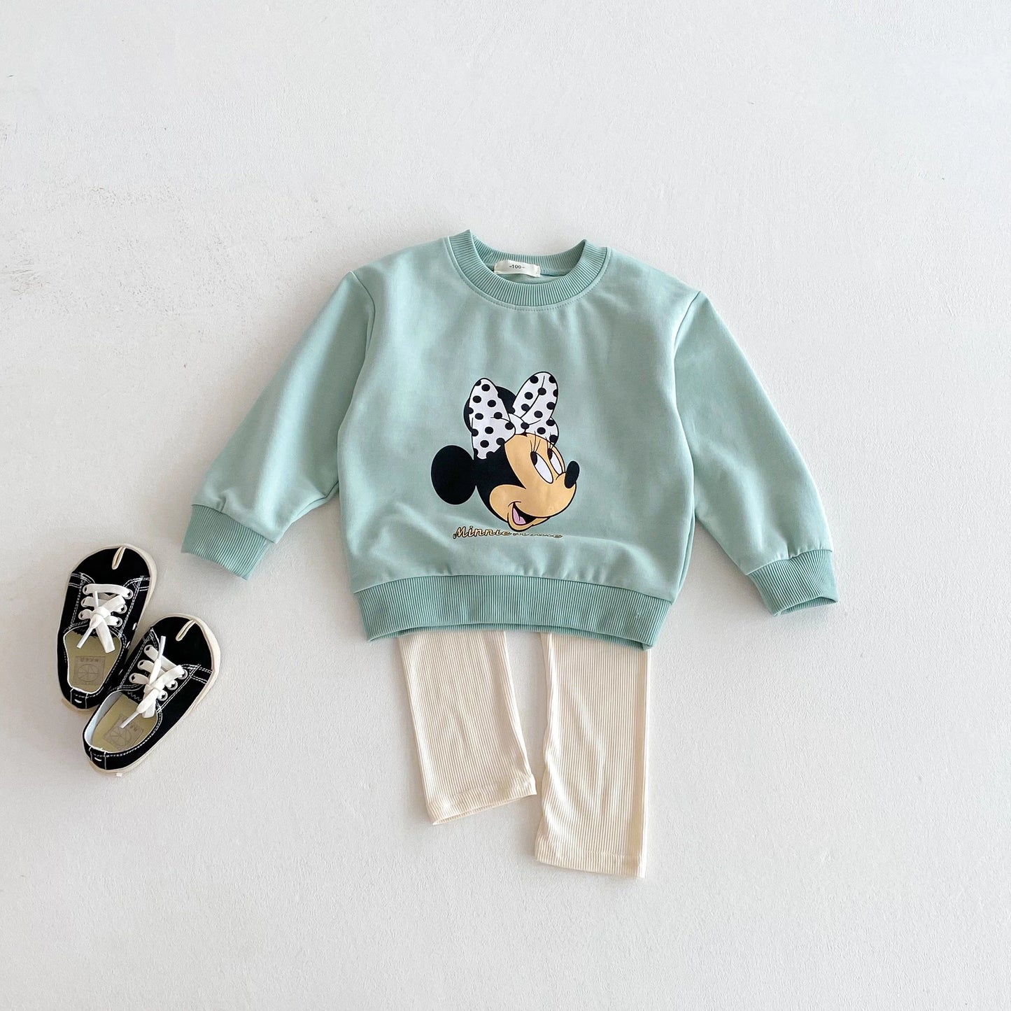 Children's outfit with a light blue sweatshirt featuring a cartoon character and beige pants on a white background.