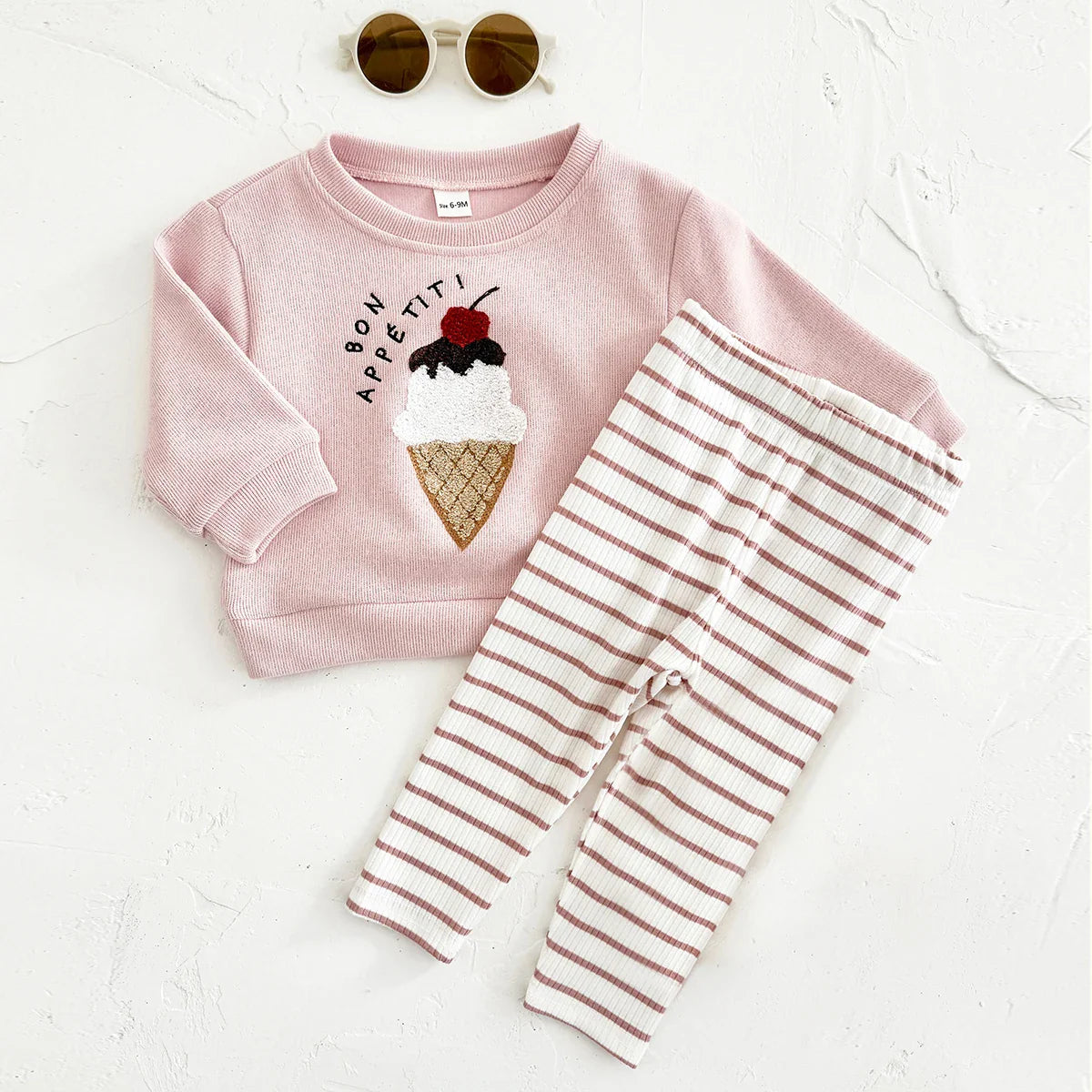Pink sweatshirt with ice cream cone design and striped pants on a white background