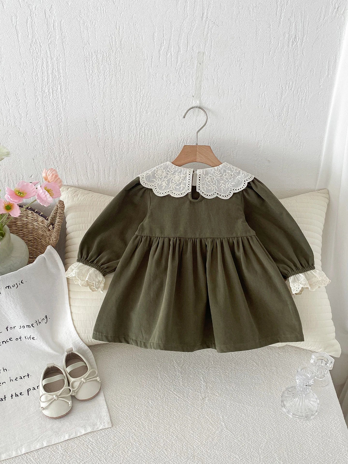Green dress with lace collar on a hanger against a white wall.