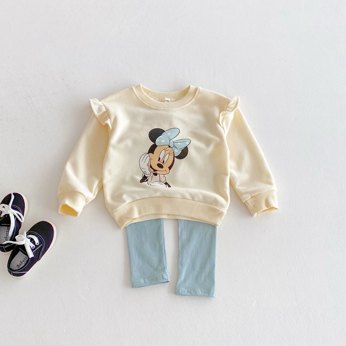 Children's outfit with a yellow sweatshirt featuring a cartoon character and light blue pants on a white background.