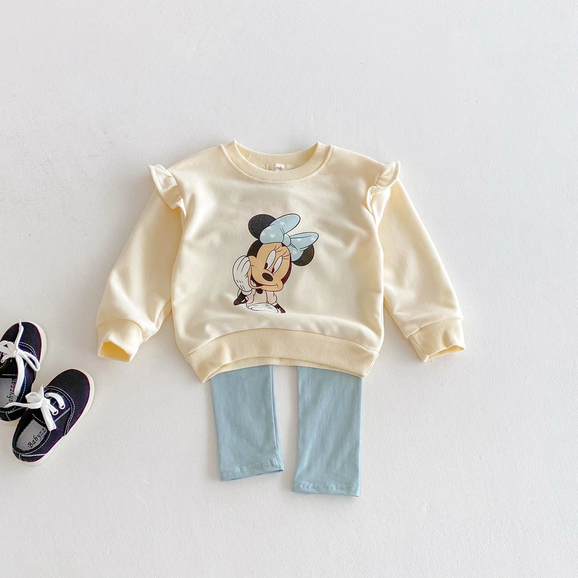 Children's outfit with a yellow sweatshirt featuring a cartoon character and light blue pants on a white background.