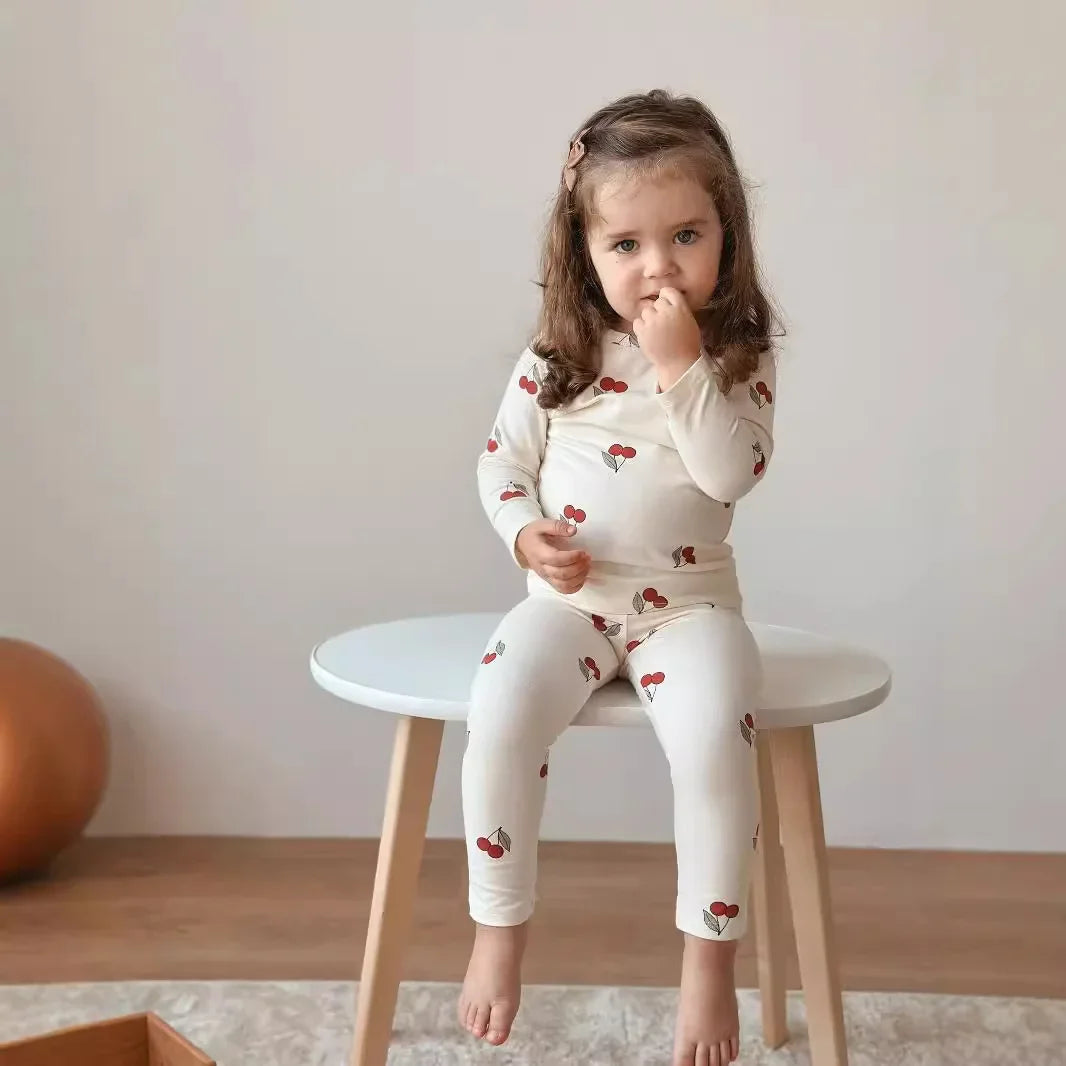 Young girl sitting on a small stool wearing a white outfit with red patterns.