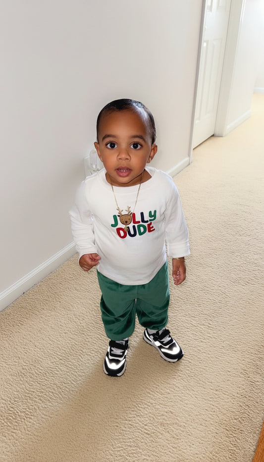 Child wearing a white shirt with colorful text and green pants standing on a carpeted floor.