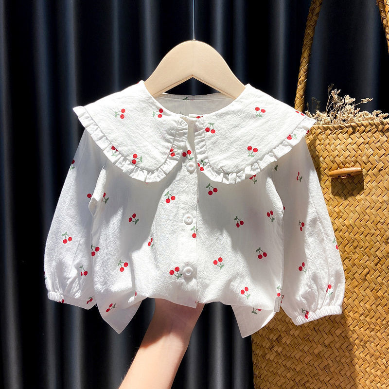 White baby blouse with large frilled collar and red cherry print, hanging on wooden hanger
