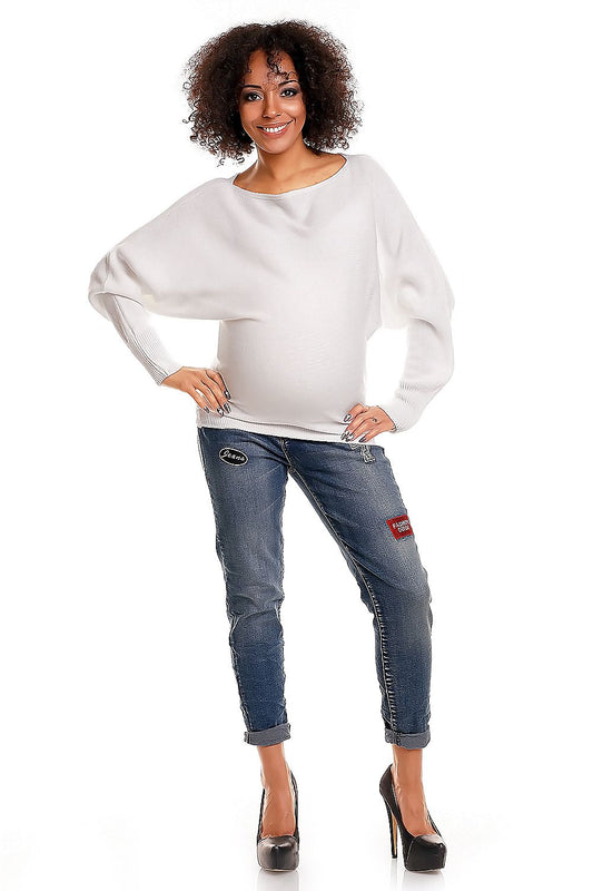 Woman wearing a white sweater and blue jeans with patches on a white background