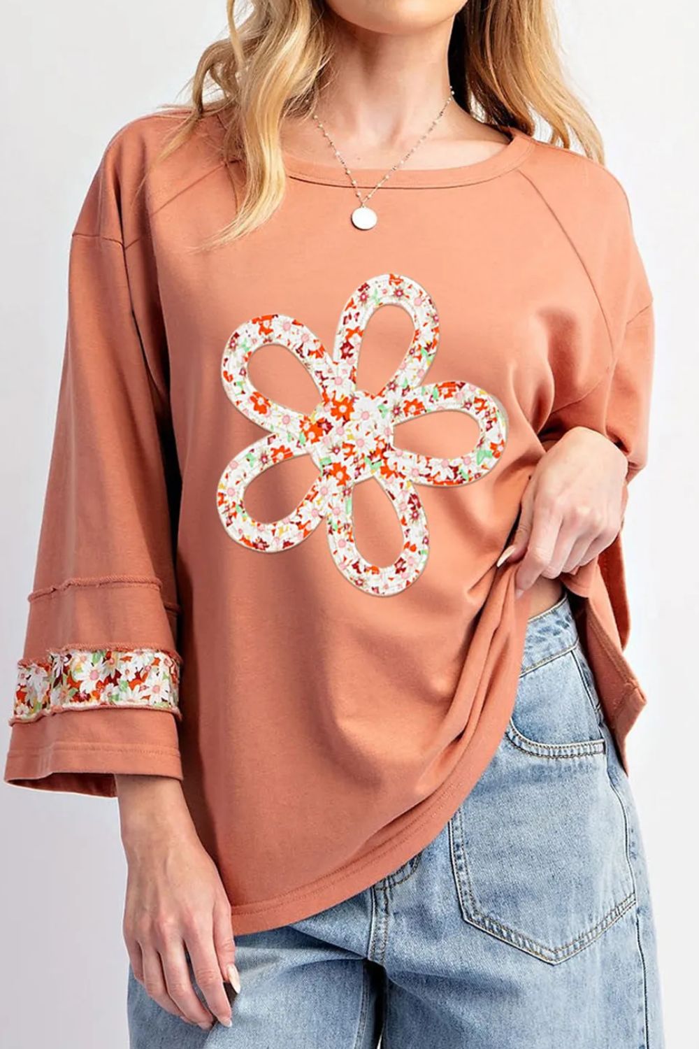 Person wearing a brown top with a floral design and blue jeans on a white background