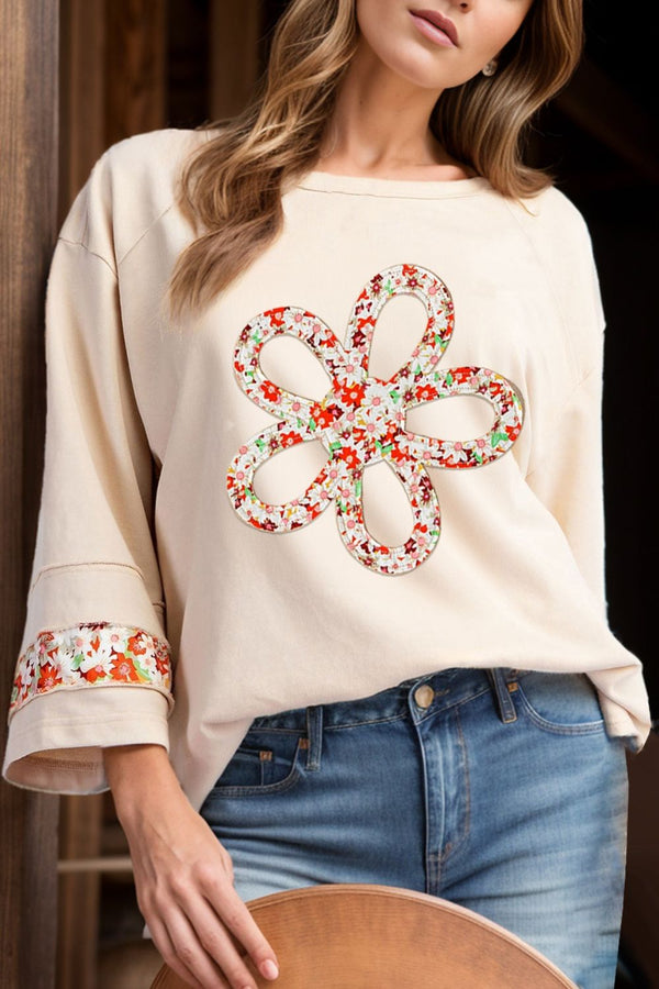 Woman wearing a beige sweater with floral embellishments and blue jeans.