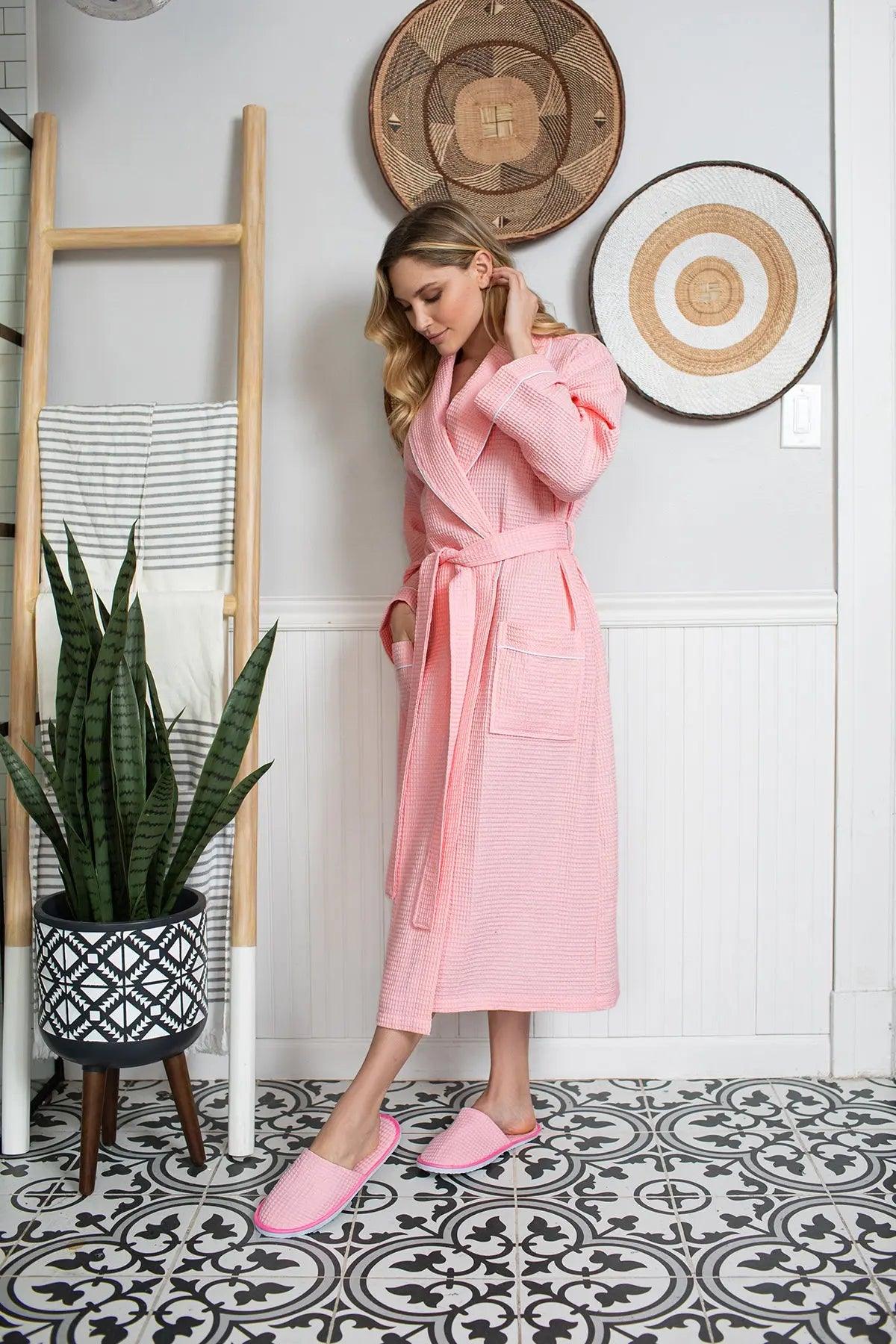 Woman in a pink robe standing in a room with decorative elements and a plant.