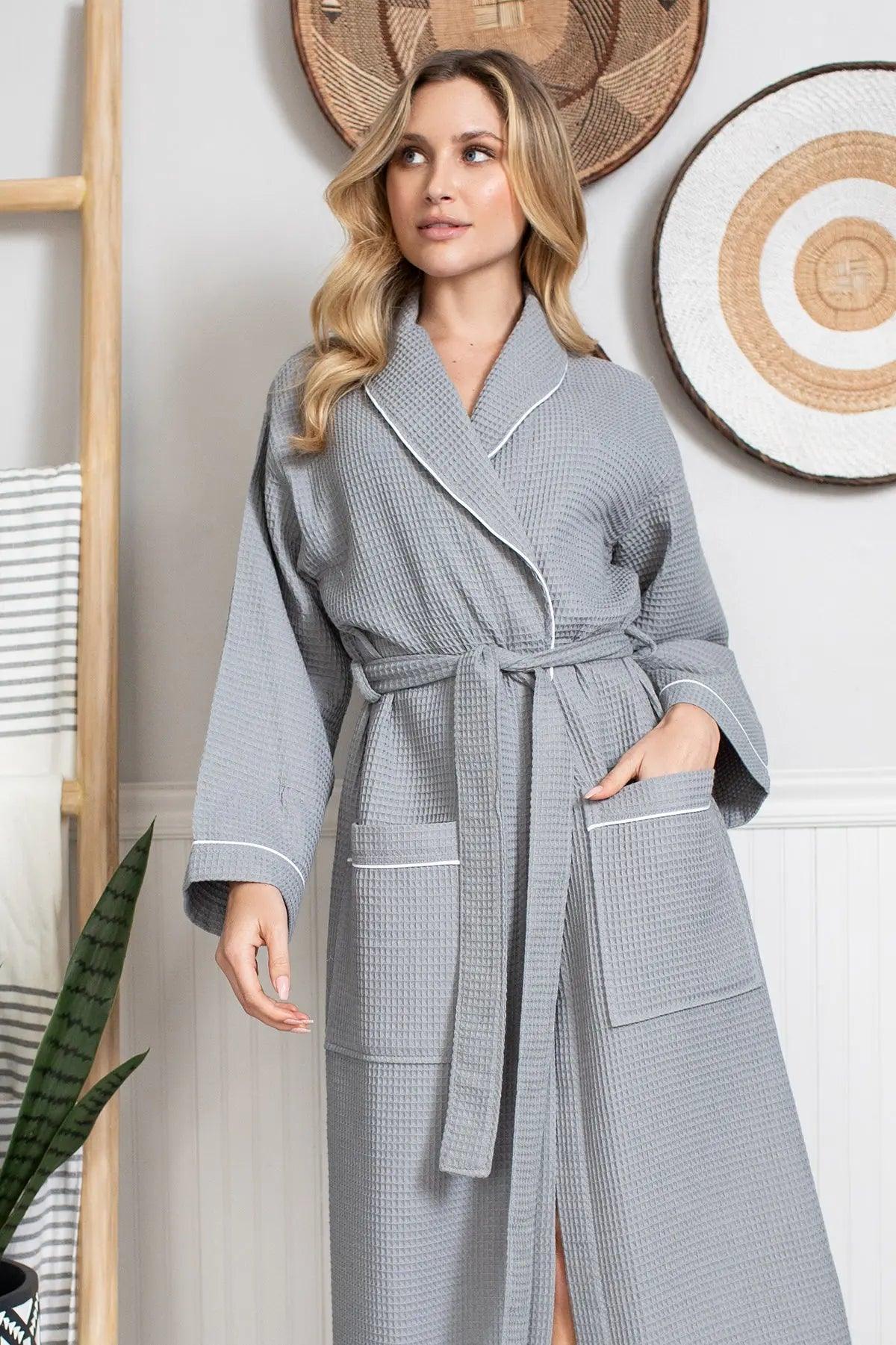 Woman wearing a gray robe with white trim in a room with decorative items on the wall.